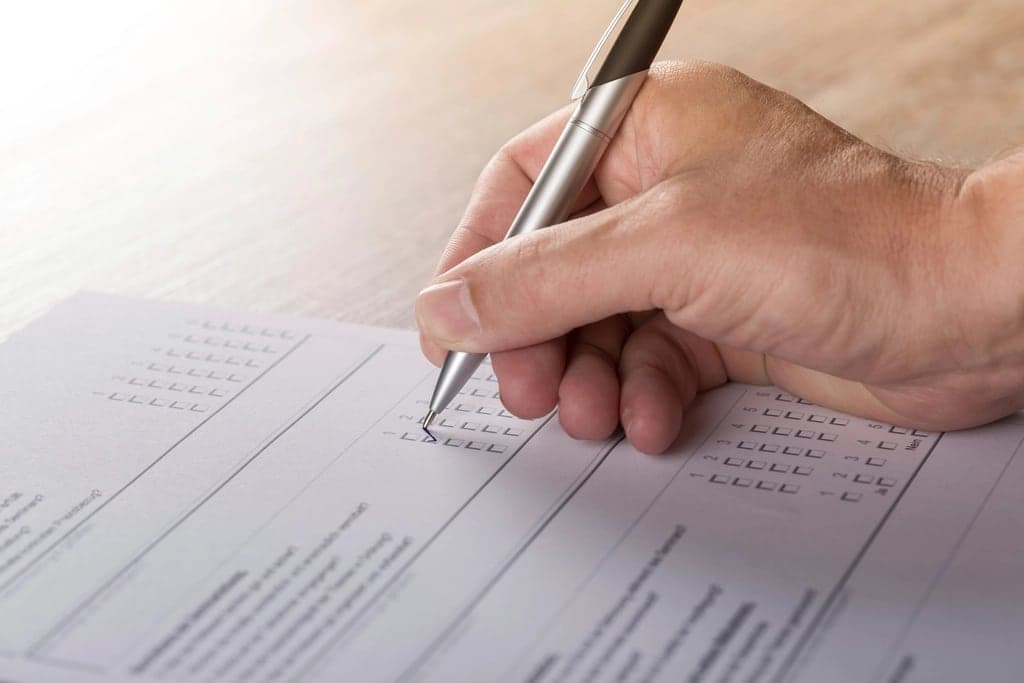 A hand ticking boxes on a paper form with a pen